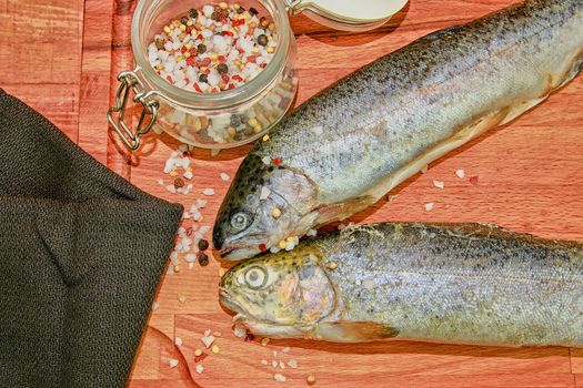 Two raw rainbow trouts with spices on wooden board. Healthy food and dieting concept. Close-up.