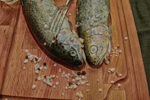 Fresh raw rainbow trouts with spices and fork on wooden board. Healthy food and dieting concept. Close-up. Add dark contrasts.