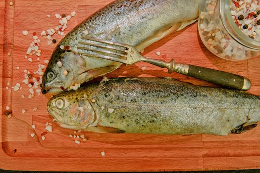 Fresh raw rainbow trouts with spices and fork on wooden board. Healthy food and dieting concept. Close-up. Add soft dark contrasts.