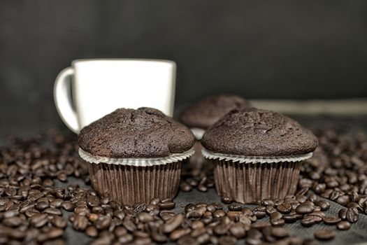 Dark muffin, cups of coffee and coffee beans on black background. Add dark contrasts. Black copy space. Coffee bar concept.