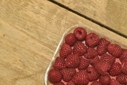 Red-fruited raspberries in plastic box on wooden background. Raspberries background. Close-up.
