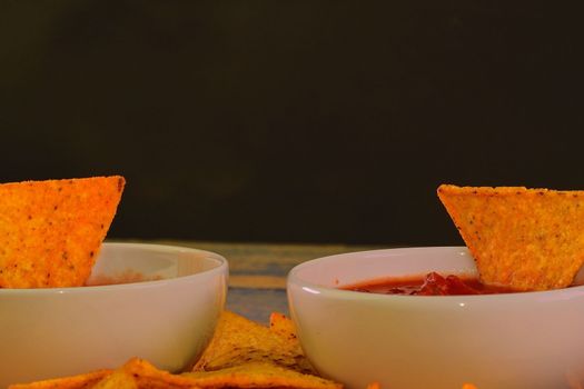 Chili corn-chips with salsa dip on wooden background. Black copy space for text.
