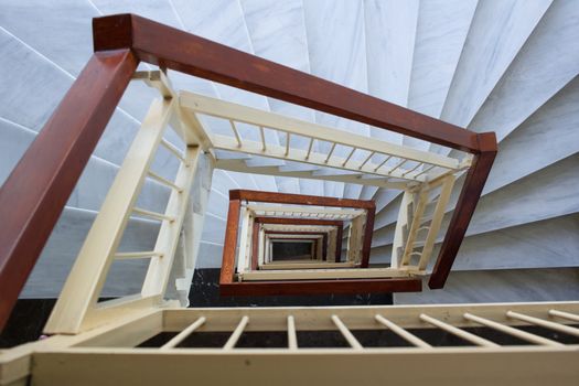 Perspective view down to spiral geometrical stairway of marble steps and wooden rails