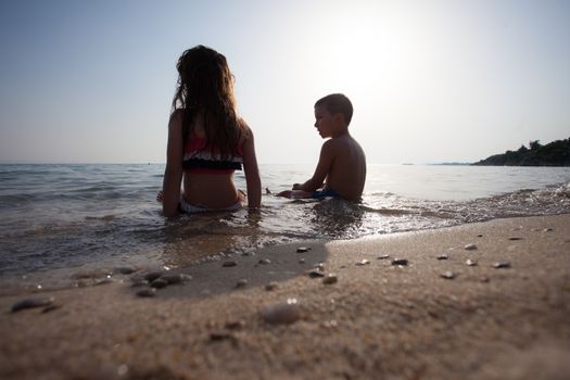 Couple of kids around six are sitting in the water of sea or ocean.