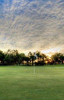 Freshly mowed green grass at dawn on a tropical golf course with a colorful sunrise sky.