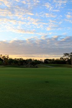 Freshly mowed green grass at dawn on a tropical golf course with a colorful sunrise sky.