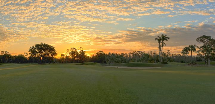 Freshly mowed green grass at dawn on a tropical golf course with a colorful sunrise sky.