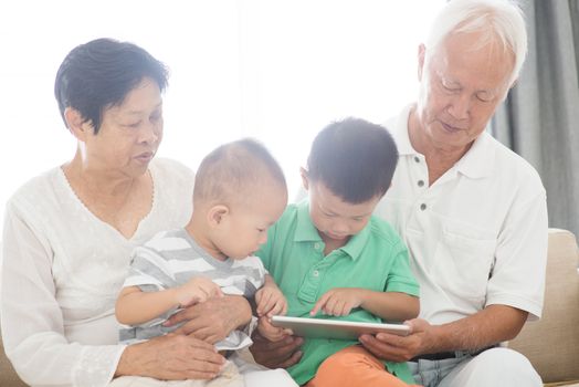 Portrait of happy Asian grandparents and grandchildren using tablet pc at home, family indoor lifestyle.