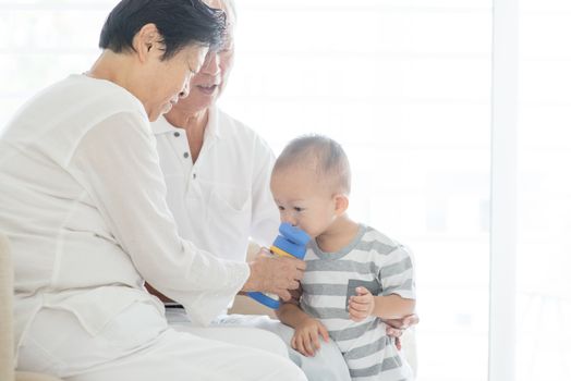Portrait of Asian grandparents feeding water to grandchild at home, family indoor lifestyle.