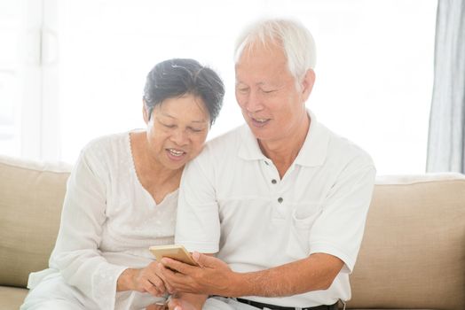Portrait of happy Asian elderly couple using smart phone at home, old senior retired people indoor lifestyle.