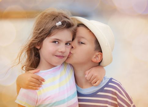 Young boy around six is kissing his sister on the chick