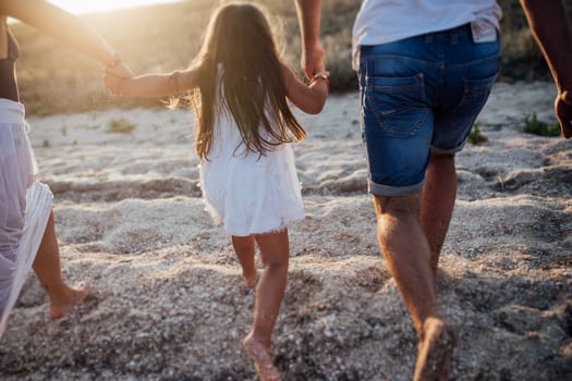 Young happy family walking along the seashore. Little girl with her parents walking on the beach and holding their hands.