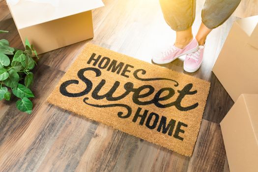 Woman in Pink Shoes and Sweats Standing Near Home Sweet Home Welcome Mat, Boxes and Plant.