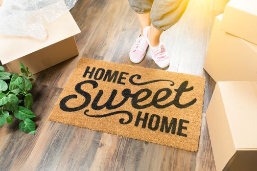 Woman in Pink Shoes and Sweats Standing Near Home Sweet Home Welcome Mat, Boxes and Plant.