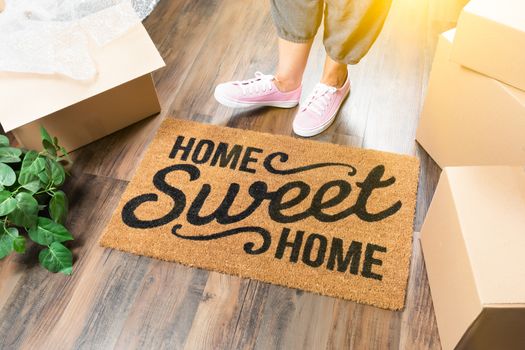 Woman in Pink Shoes and Sweats Standing Near Home Sweet Home Welcome Mat, Boxes and Plant.