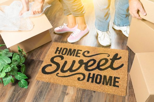 Man and Woman Unpacking Near Home Sweet Home Welcome Mat, Moving Boxes and Plant.