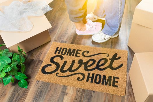 Man and Woman Standing Near Home Sweet Home Welcome Mat, Moving Boxes and Plant.