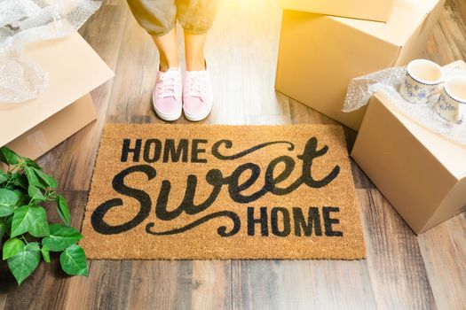 Woman in Pink Shoes and Sweats Standing Near Home Sweet Home Welcome Mat, Boxes and Plant.