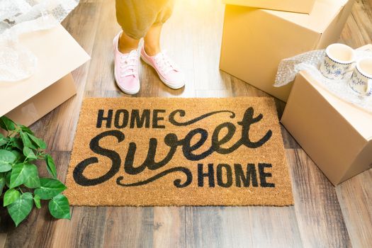 Woman in Pink Shoes and Sweats Standing Near Home Sweet Home Welcome Mat, Boxes and Plant.