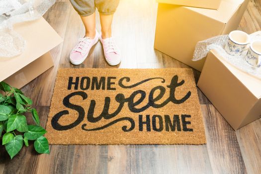 Woman in Pink Shoes and Sweats Standing Near Home Sweet Home Welcome Mat, Boxes and Plant.