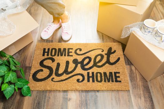 Woman in Pink Shoes and Sweats Standing Near Home Sweet Home Welcome Mat, Boxes and Plant.