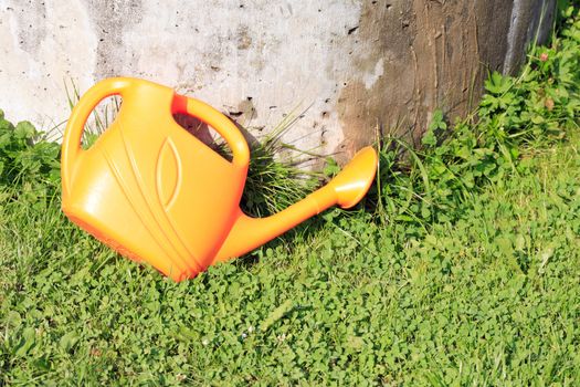Plastic yellow watering can on green grass in garden
