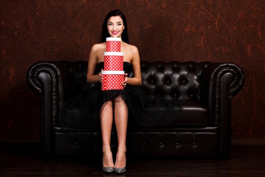 Pretty woman is sitting on the leather sofa with stack of presents