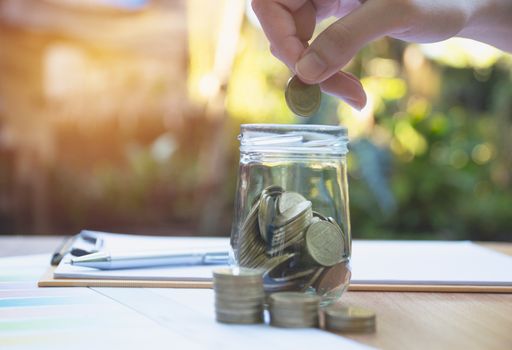 Woman process and drop coin into the glass with stack coins and calculator. Woman working on table.