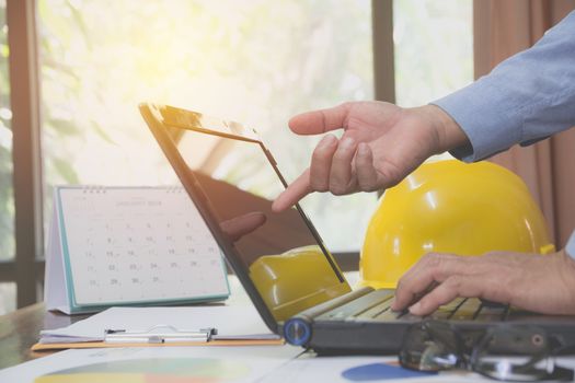 Architect engineer using laptop for working with yellow helmet on desk.