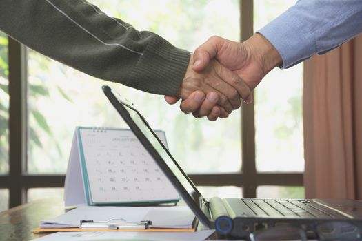 Business people shaking hands. Top view of two Business people shaking hands while standing on the desk with laptop.