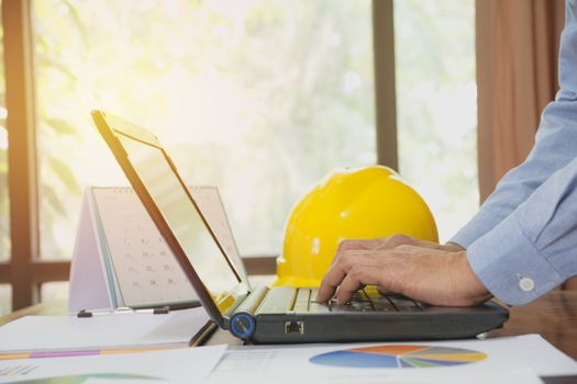 Architect engineer using laptop for working with yellow helmet on desk.
