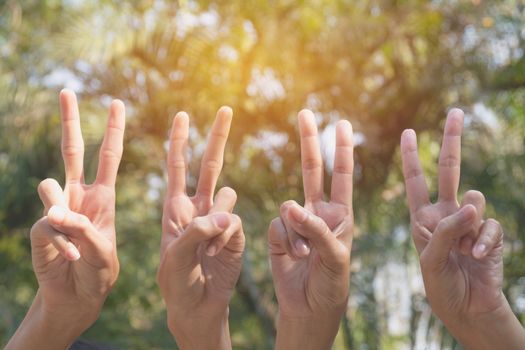 Hand of people shows the gesture of victory on nature background.