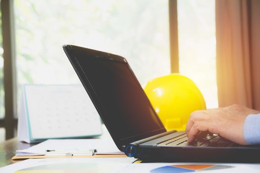 Architect engineer using laptop for working with yellow helmet on desk.