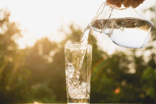 Person pouring water from pitcher to glass on nature background