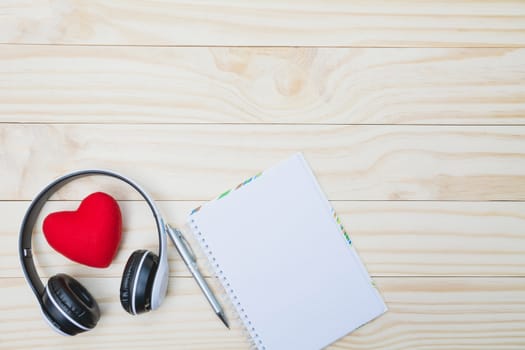 Red heart with headset, pen and empty note on wooden table with copy space for valentine day concept.