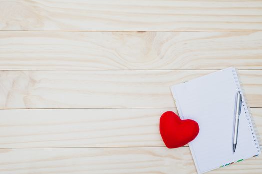 Red heart with pen and empty note on wooden table with copy space for valentine day concept.