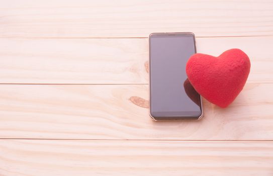 Red heart with smart phone on wooden table for valentine day concept.