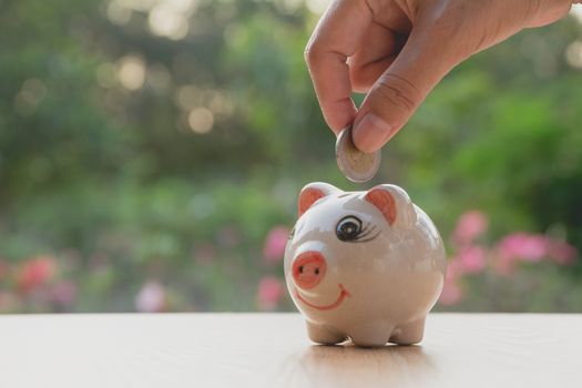 Hand of man holding coin and drop into the piggy bank. Financial stock market in accounting market economy analysis.