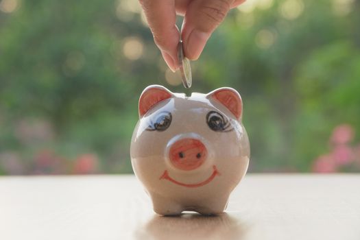 Hand of man holding coin and drop into the piggy bank. Financial stock market in accounting market economy analysis.