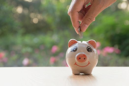 Hand of man holding coin and drop into the piggy bank. Financial stock market in accounting market economy analysis.