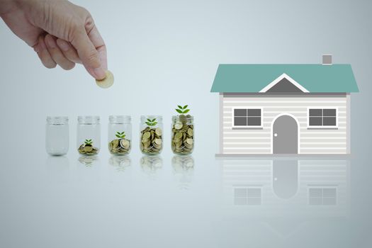 Hand of man holding coin and drop into the glass. Save money for a house concept.
