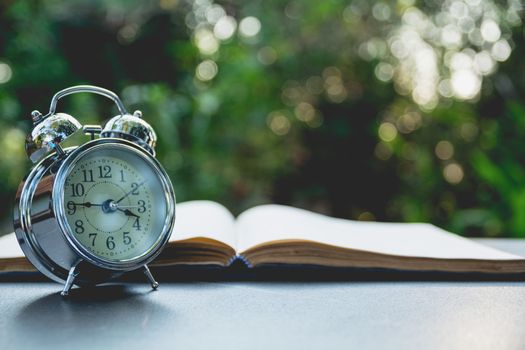 Open book with alarm clock. Book open on old wooden table on nature background.