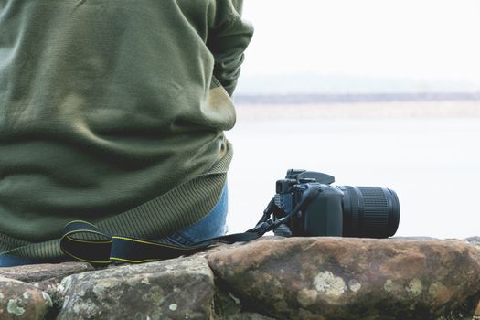 Woman sitting on the rock with camera on river background.