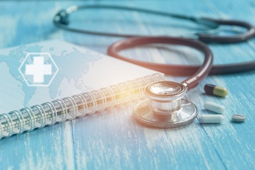 Medical stethoscope with pharmaceutical medicine pills and capsules on wooden table.