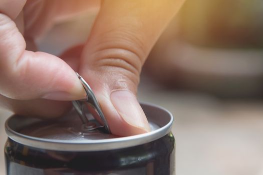 Hand opening an iron can. Can with a drink of cola.