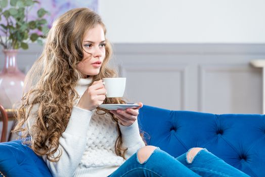 horizontal portrait of a beautiful young woman with a cup of coffee on the couch