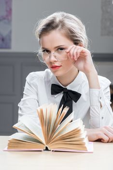 charming successful businesswoman in glasses with a book at the table sits