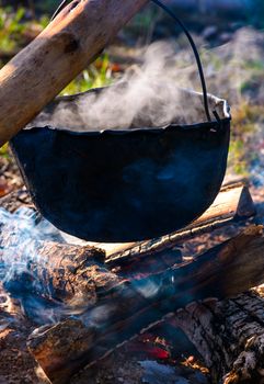 cauldron in steam and smoke on open fire. outdoor cooking concept. old fashioned way to make food