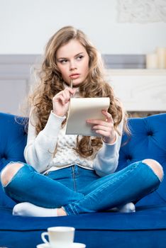 vertical portrait of a pensive girl with a notebook sitting on the couch