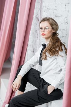 stylish successful businesswoman in glasses sits near a window and poses